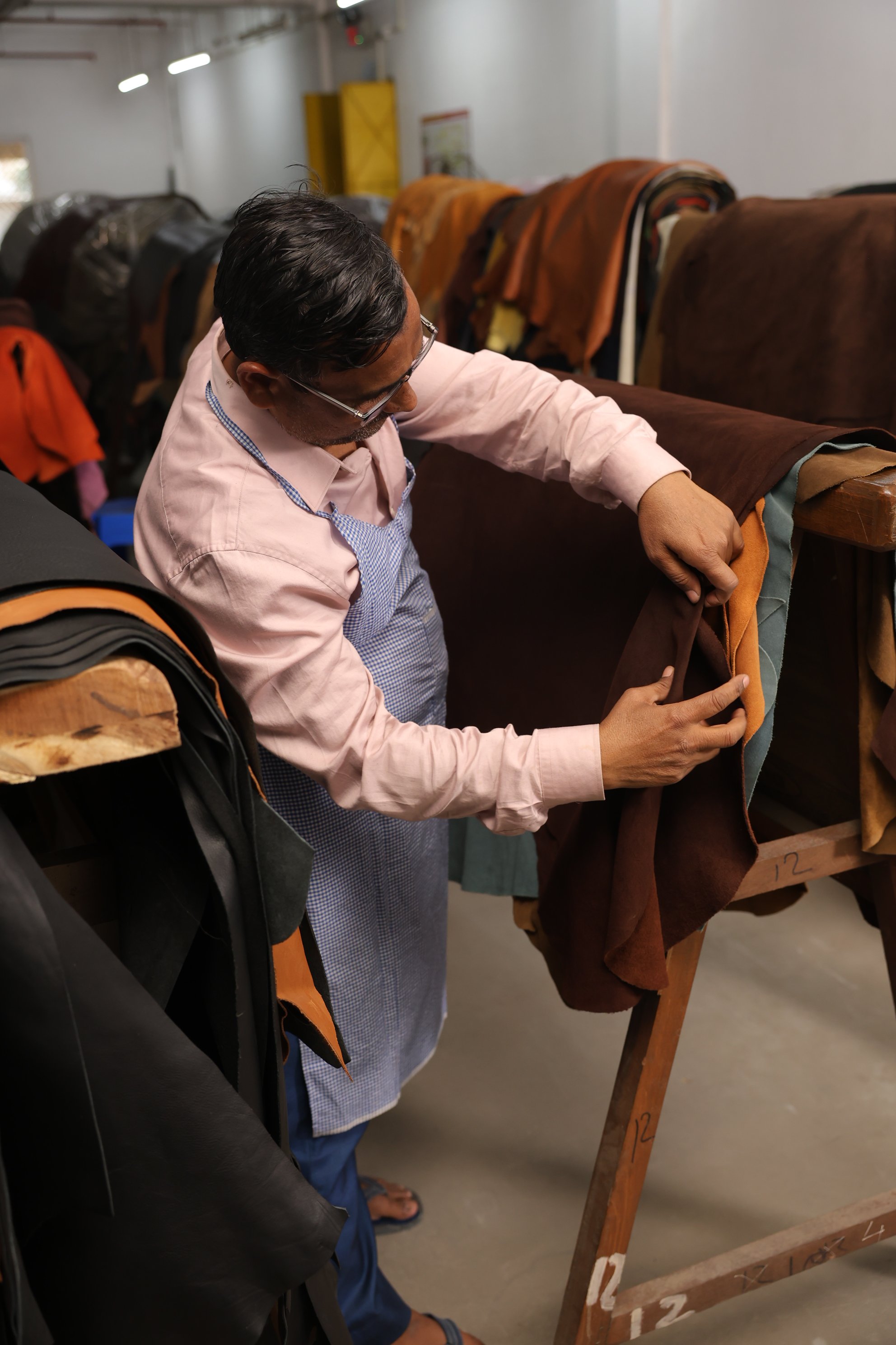 Master artisan selecting certified leather hides and grading texture inside the materials workshop